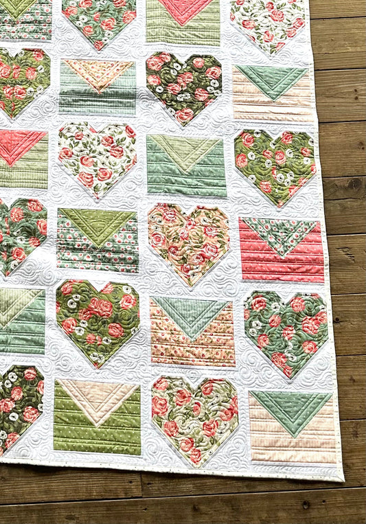 Colorful heart-patterned quilt featuring floral and geometric designs in green, pink, and cream fabrics.