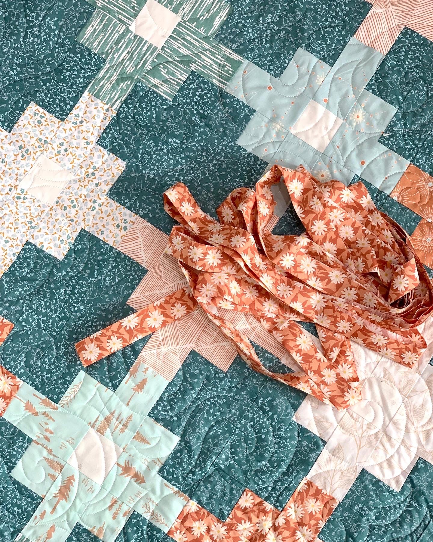 Colorful quilt featuring teal, green, and peach patterns with floral fabric strips for sewing.