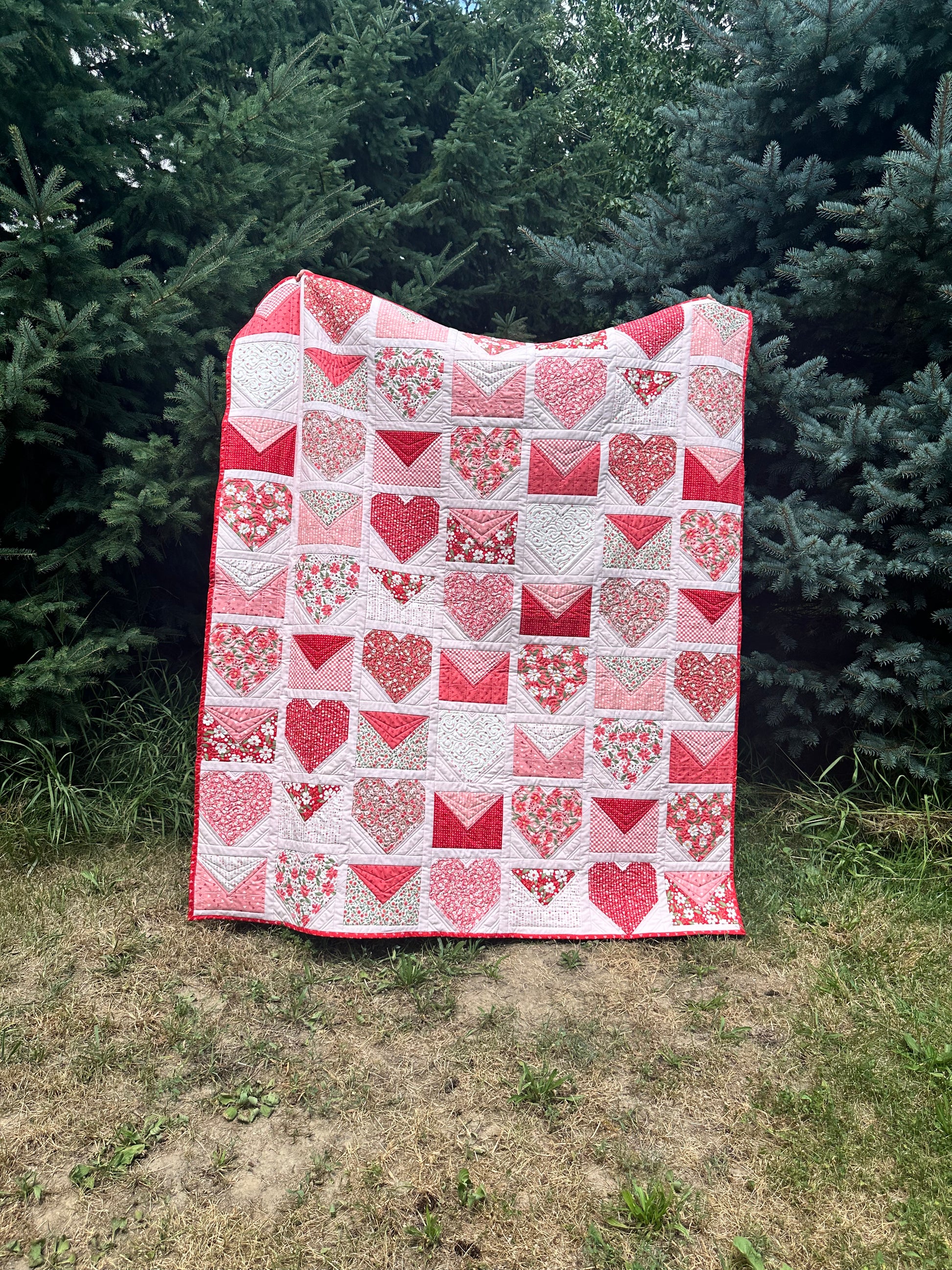 Handmade quilt featuring red and pink hearts and envelopes, perfect for cozying up or gifting.