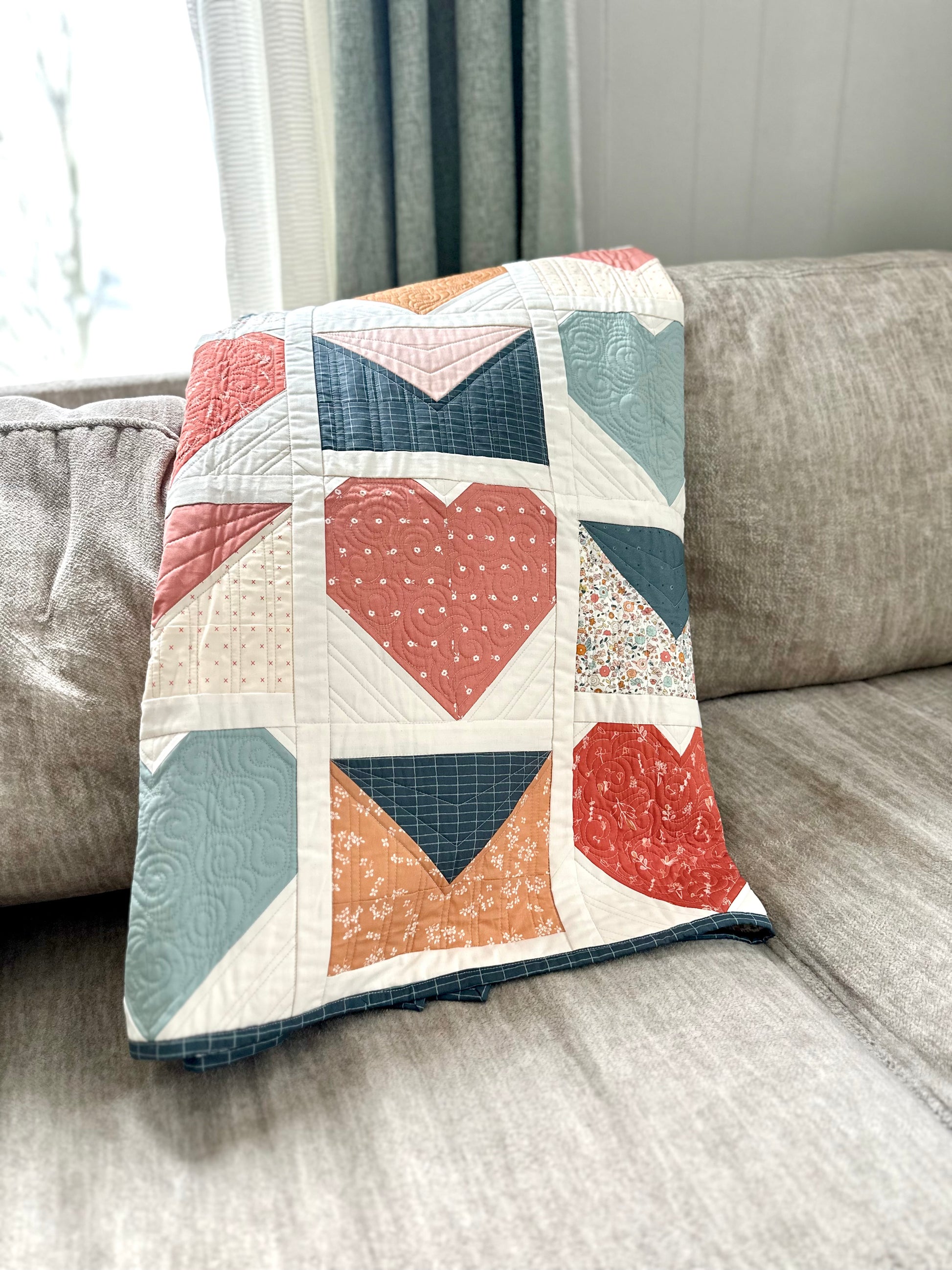 Colorful heart-themed quilt in coral, blue, and white, made from soft fabric for cozy home decor.