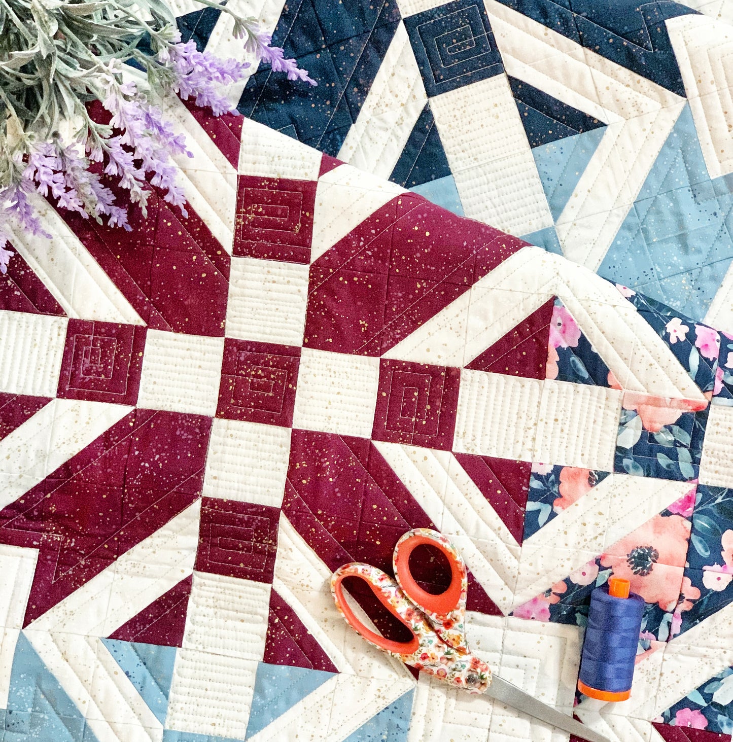 Colorful quilt featuring navy, burgundy, and cream fabrics with floral accents, scissors and thread displayed.