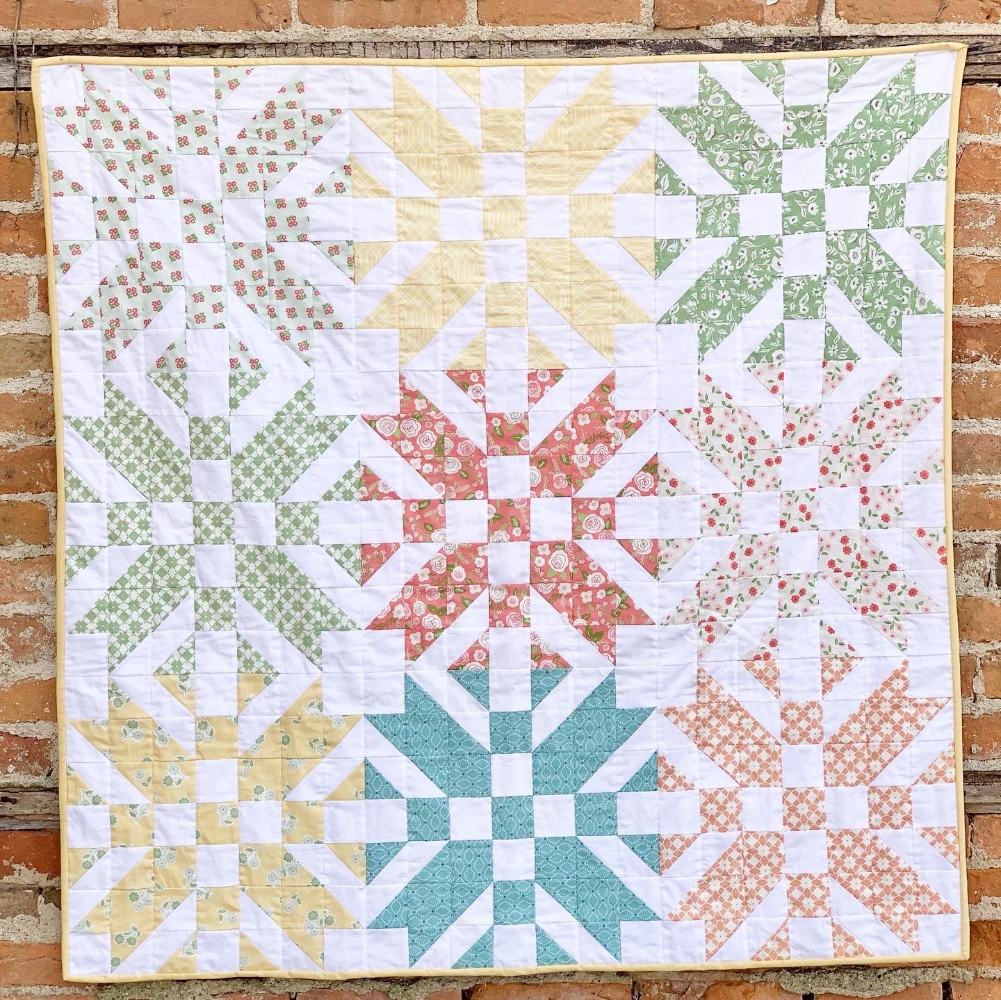 Colorful quilt with floral and geometric patterns in pastel hues, made from cotton fabric.