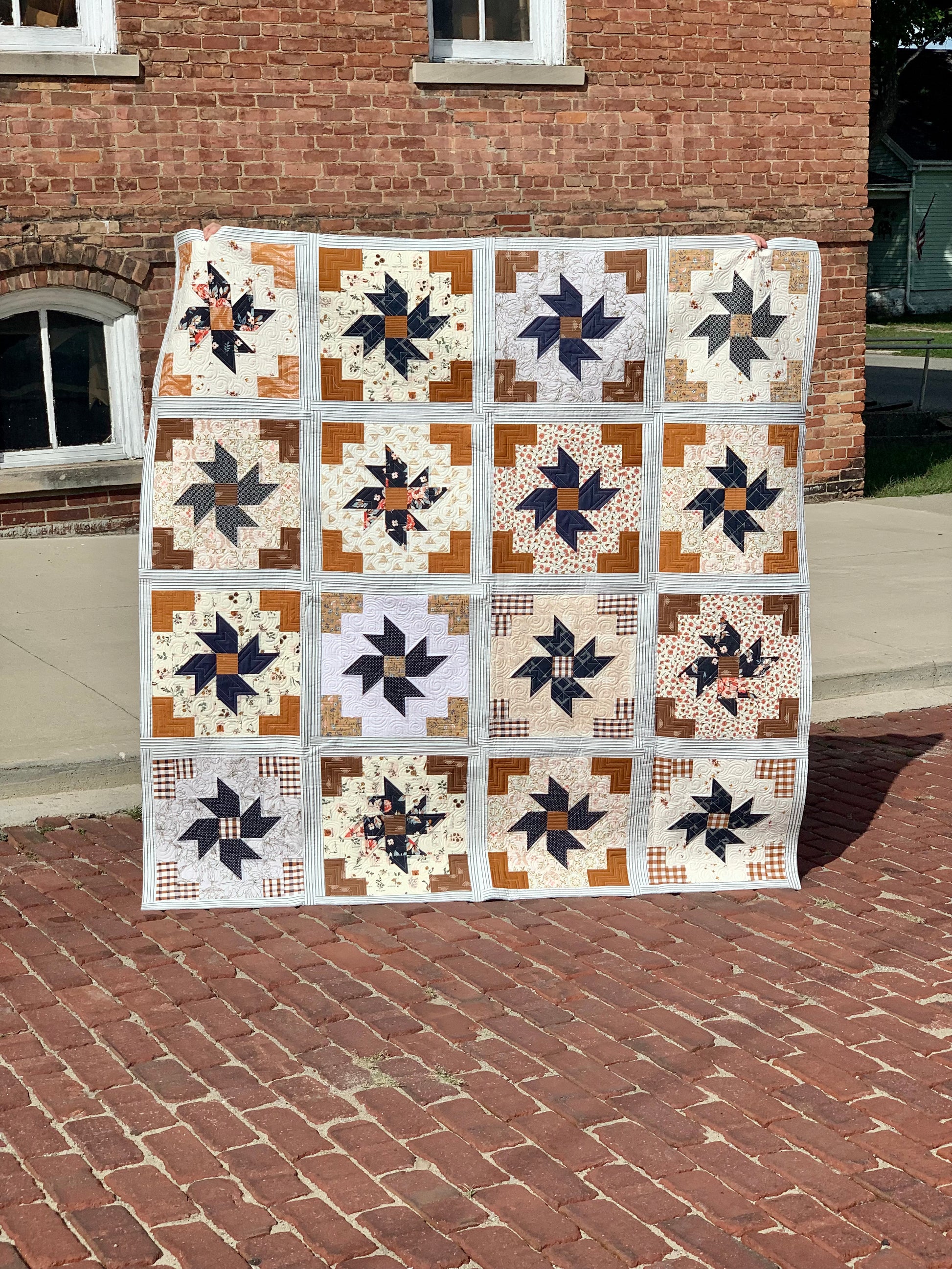 Handmade quilt with star patterns in navy, cream, and brown tones, perfect for home decor or gifting.