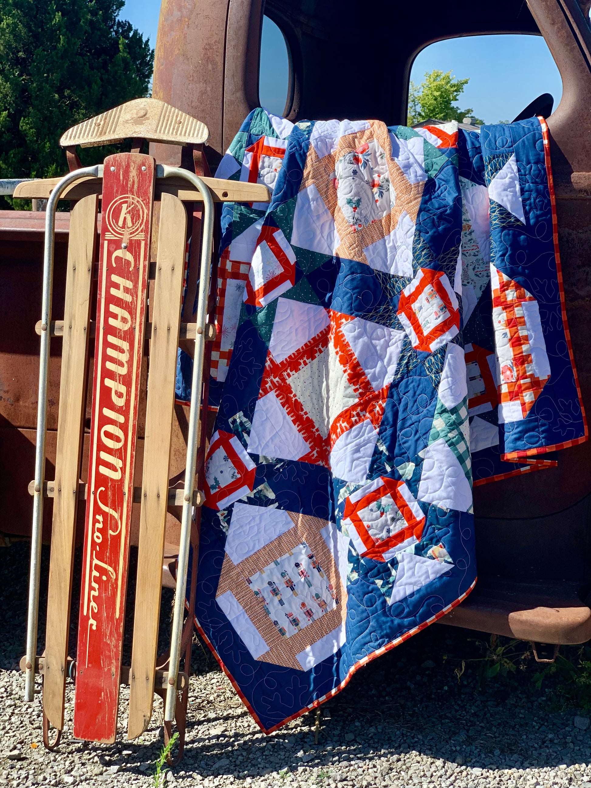 Colorful patchwork quilt in navy and white, featuring festive patterns, draped over vintage sled.
