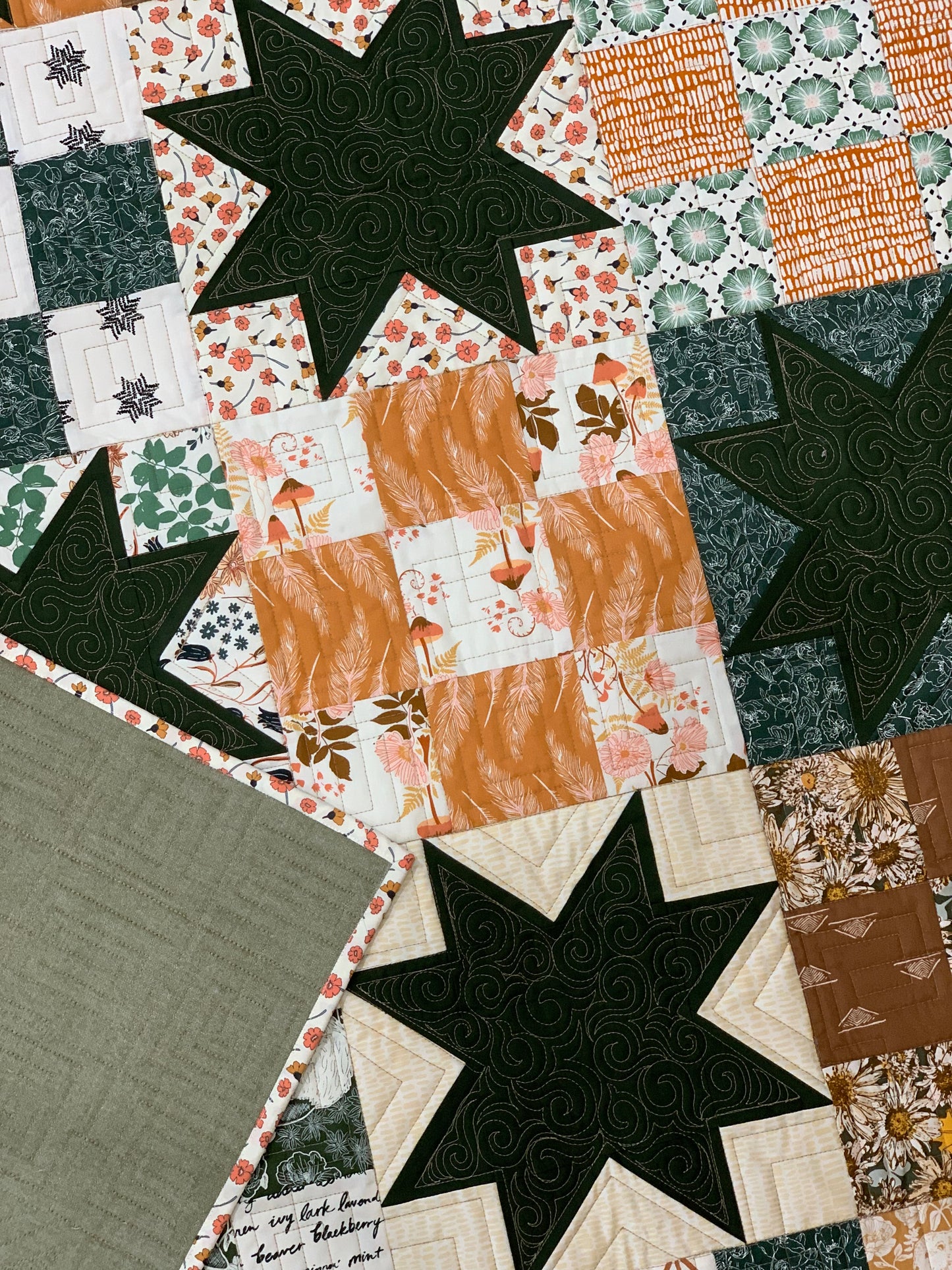 Colorful quilt featuring floral and star patterns in green, orange, and cream fabrics, perfect for home décor.