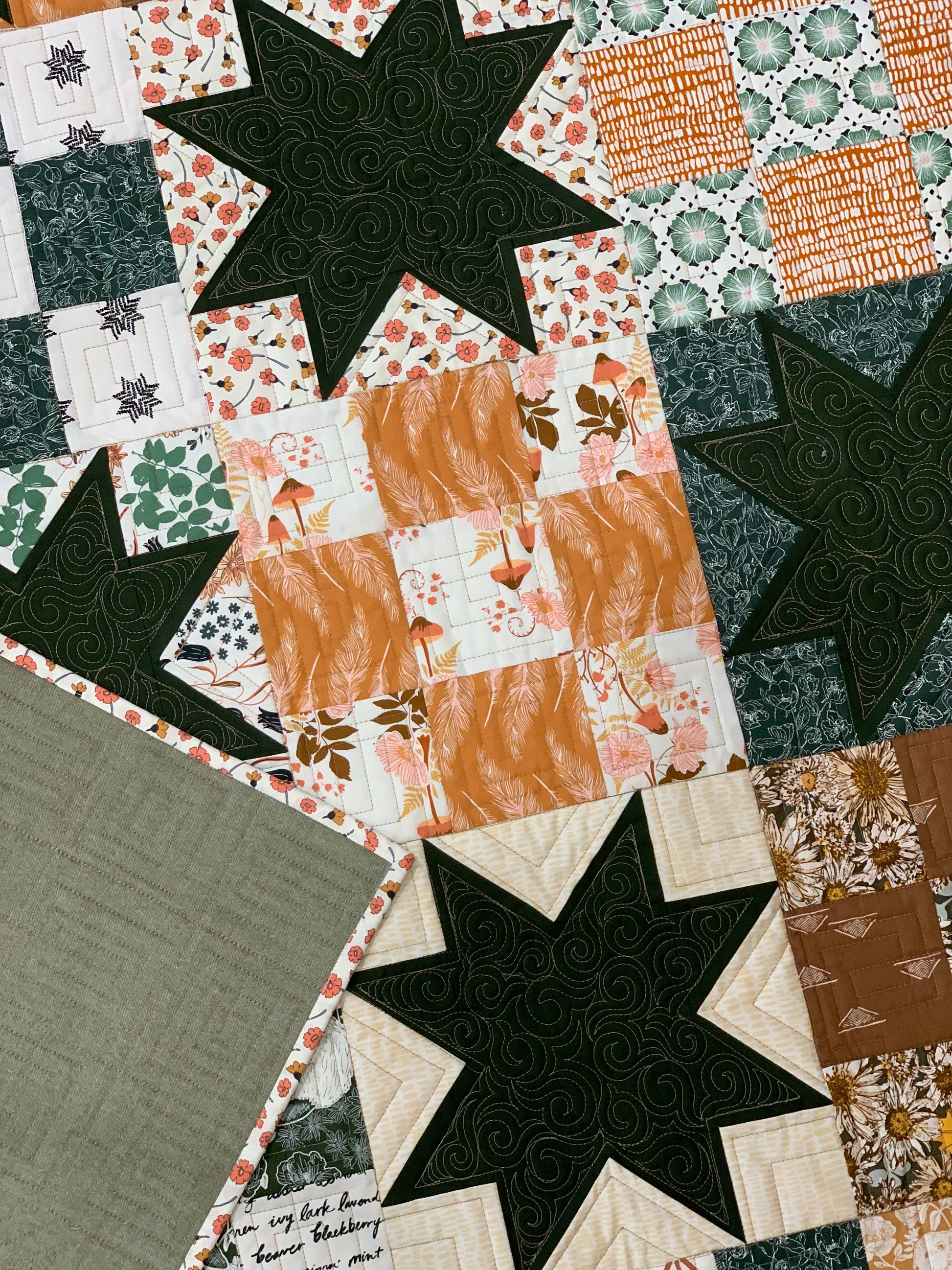 Colorful quilt featuring floral and star patterns in green, orange, and cream fabrics, perfect for home décor.