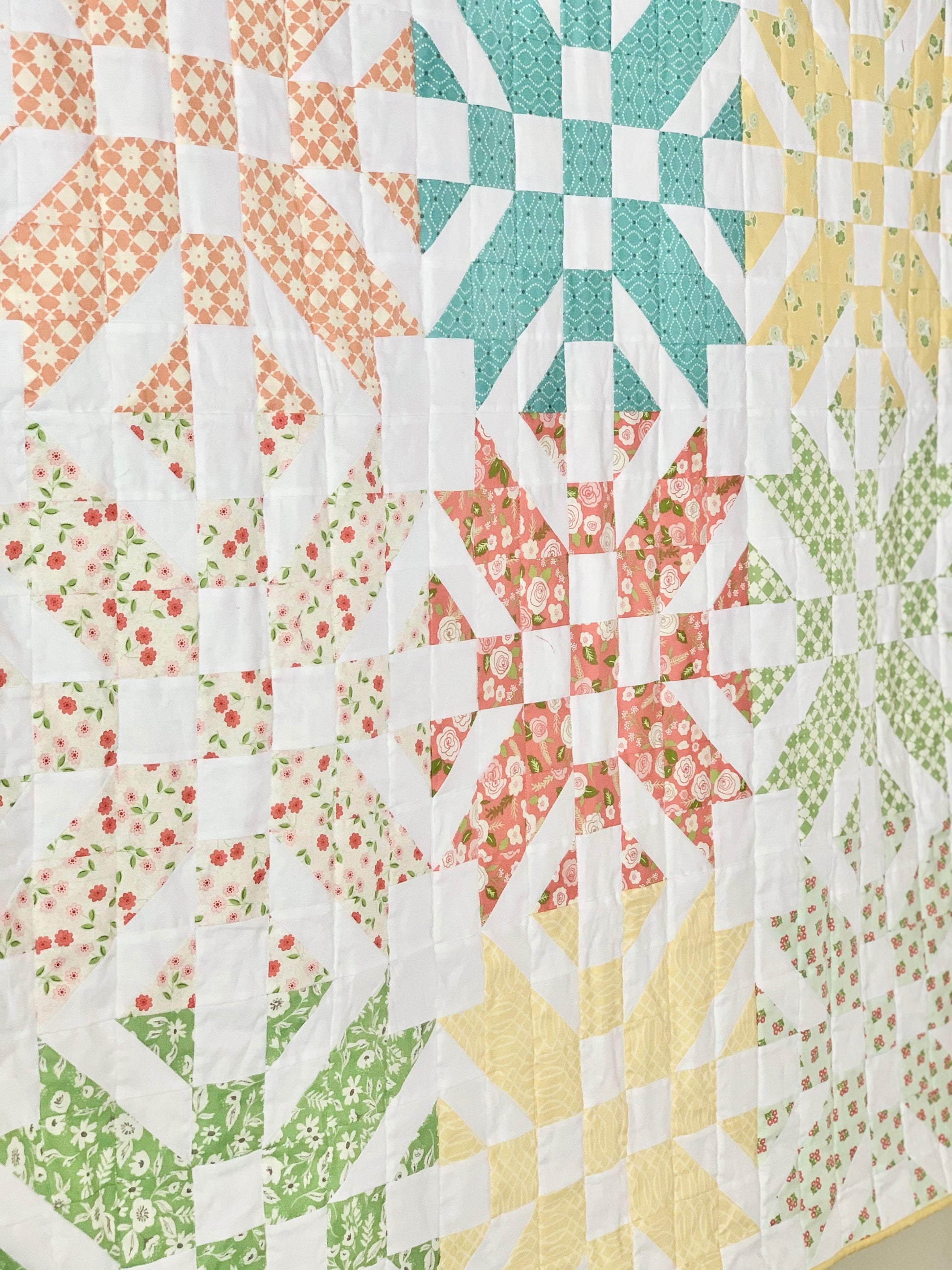 Colorful quilt featuring floral and geometric patterns in peach, teal, yellow, and green fabrics.
