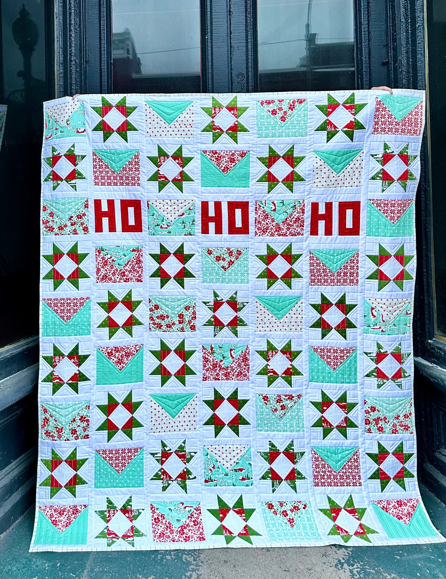 Colorful Christmas quilt featuring red, green, and aqua patterns with festive 'HO HO HO' design.