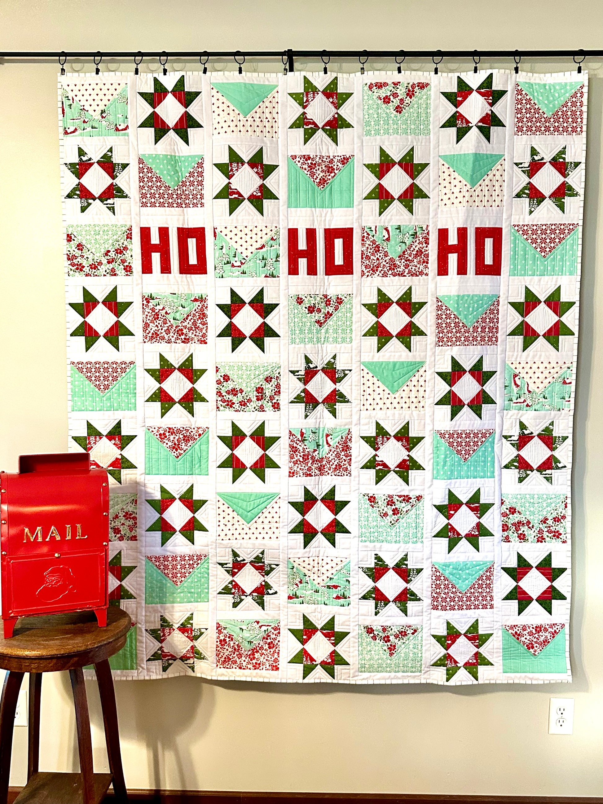 Colorful quilted wall hanging featuring star patterns in red, green, and aqua fabrics with 'HO HO' text.