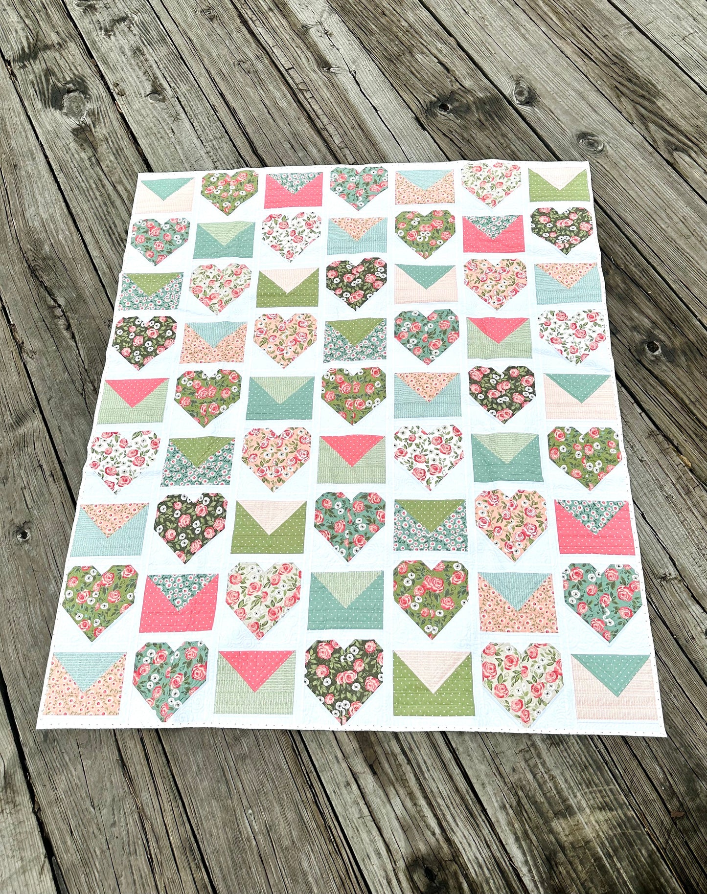 Colorful heart-patterned quilt in floral designs, featuring pastel colors on a wooden surface.