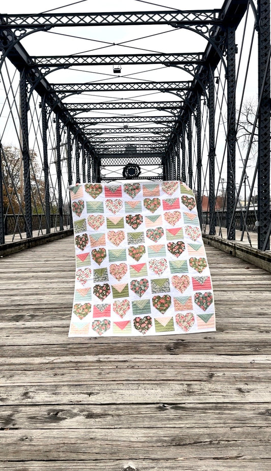 Colorful heart-patterned quilt made from cotton, displayed on a wooden bridge, showcasing floral designs.