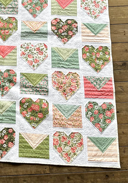 Colorful quilt featuring heart and envelope patterns in floral fabrics, perfect for home decor.
