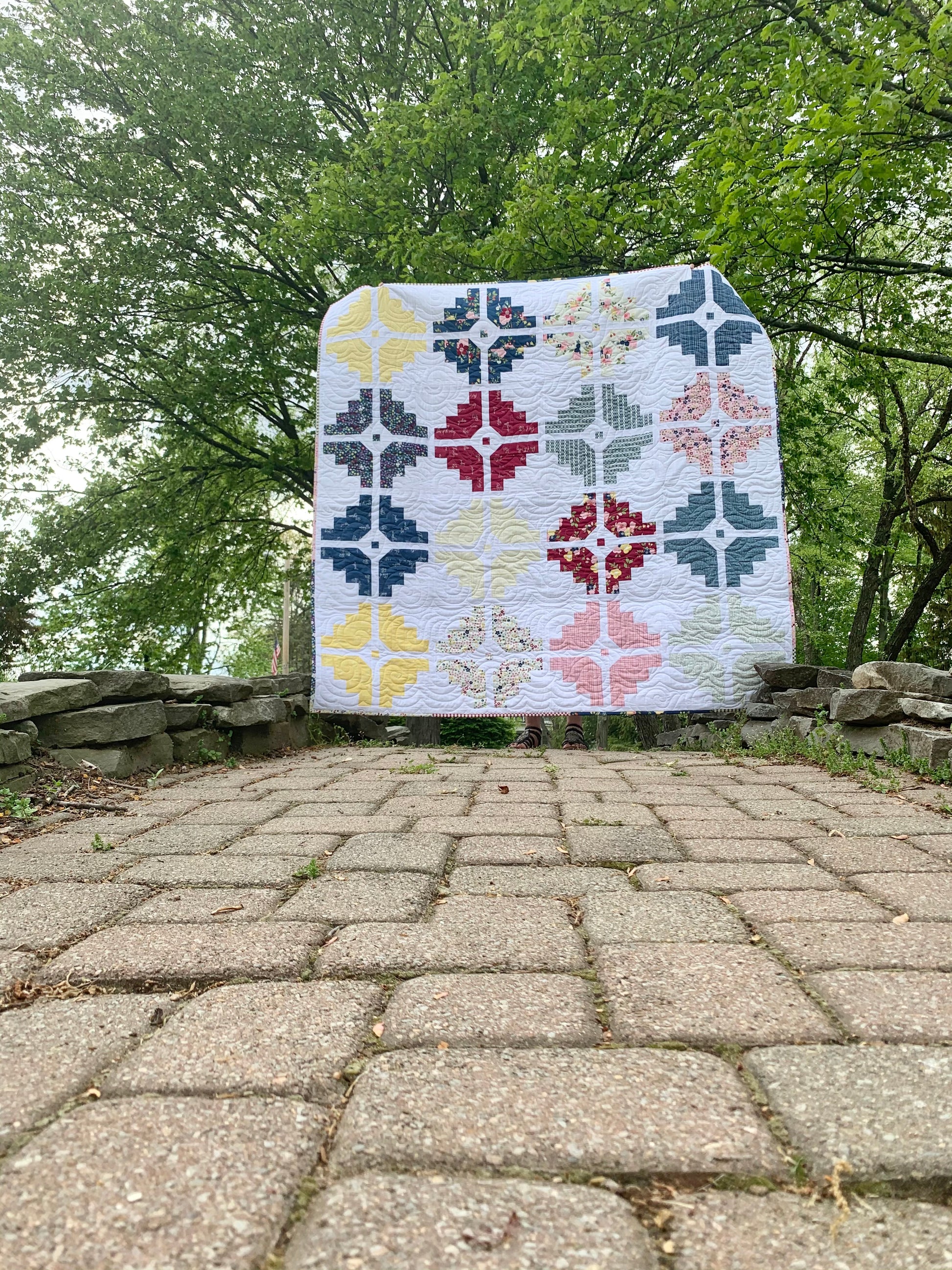Colorful quilt featuring geometric patterns in yellow, red, navy, and gray on a white background.