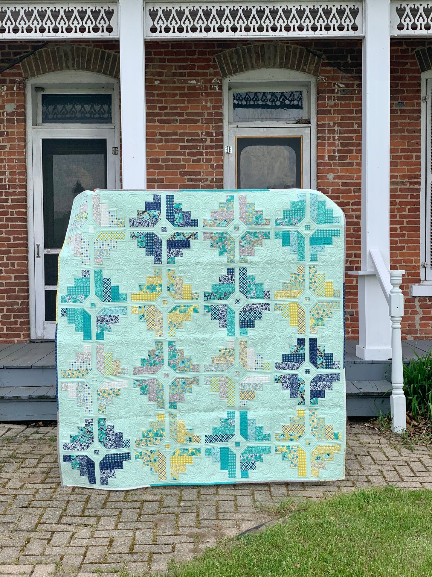 Colorful quilt featuring geometric patterns in mint green, navy, yellow, and teal fabric.
