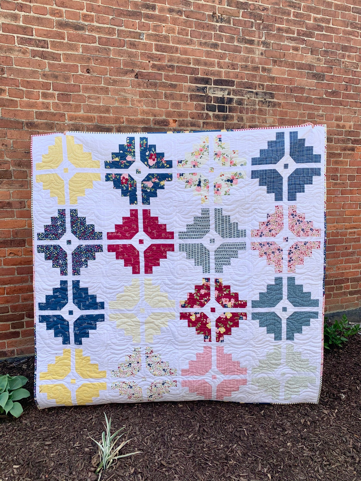 Colorful quilt with floral and geometric patterns, featuring blue, pink, yellow, and green hues.