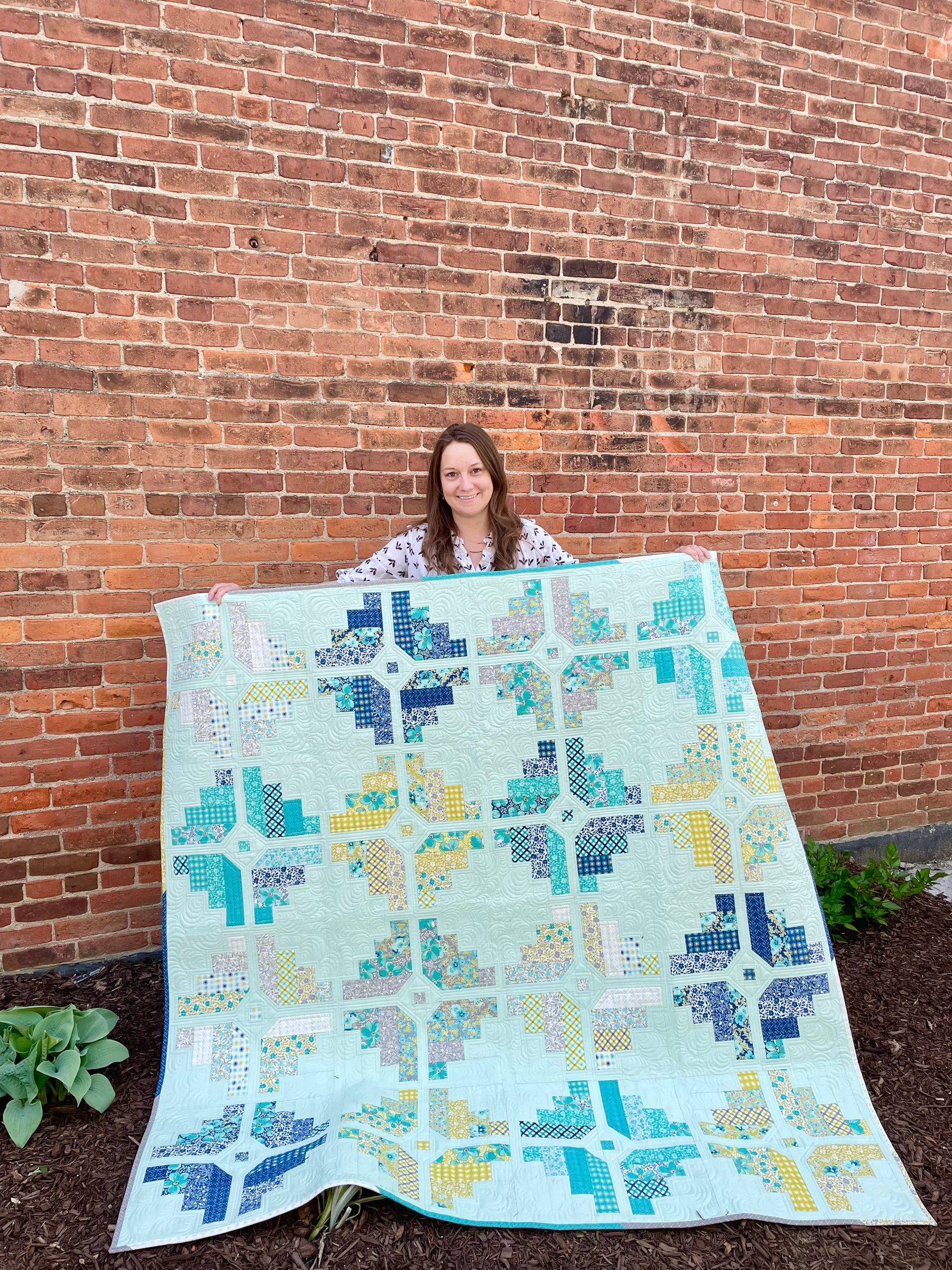 Colorful quilt with geometric patterns, featuring mint green, blue, and yellow tones, perfect for home décor.