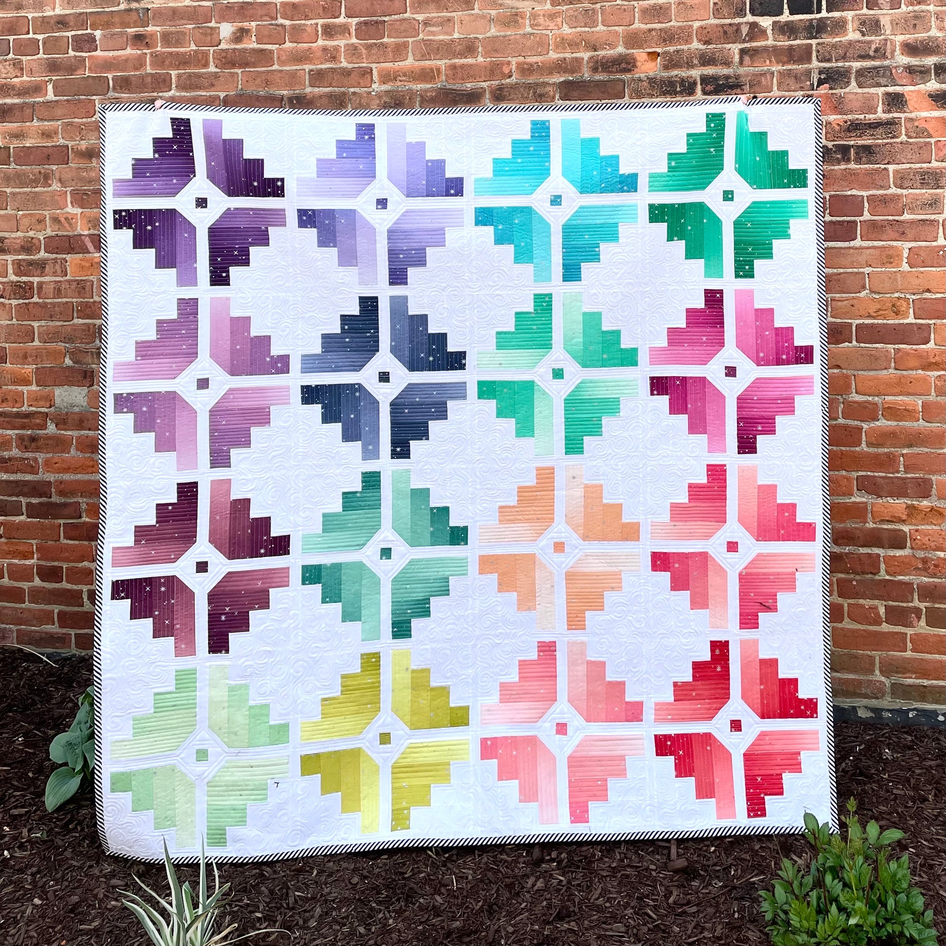 Colorful quilt featuring log cabin pattern in shades of purple, teal, pink, and green, made from cotton.