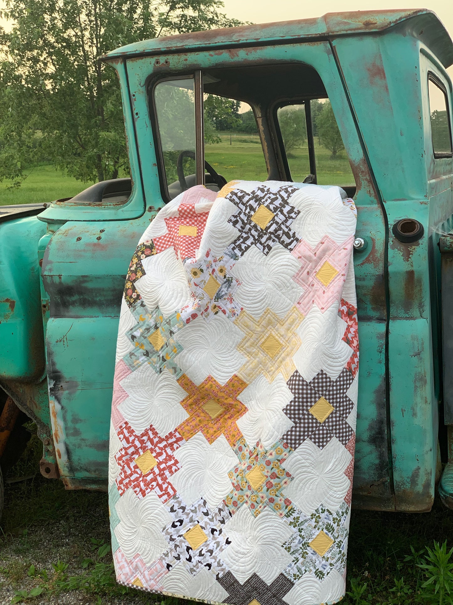 Colorful quilt with star pattern in yellow, pink, and red, draped over a vintage turquoise truck.