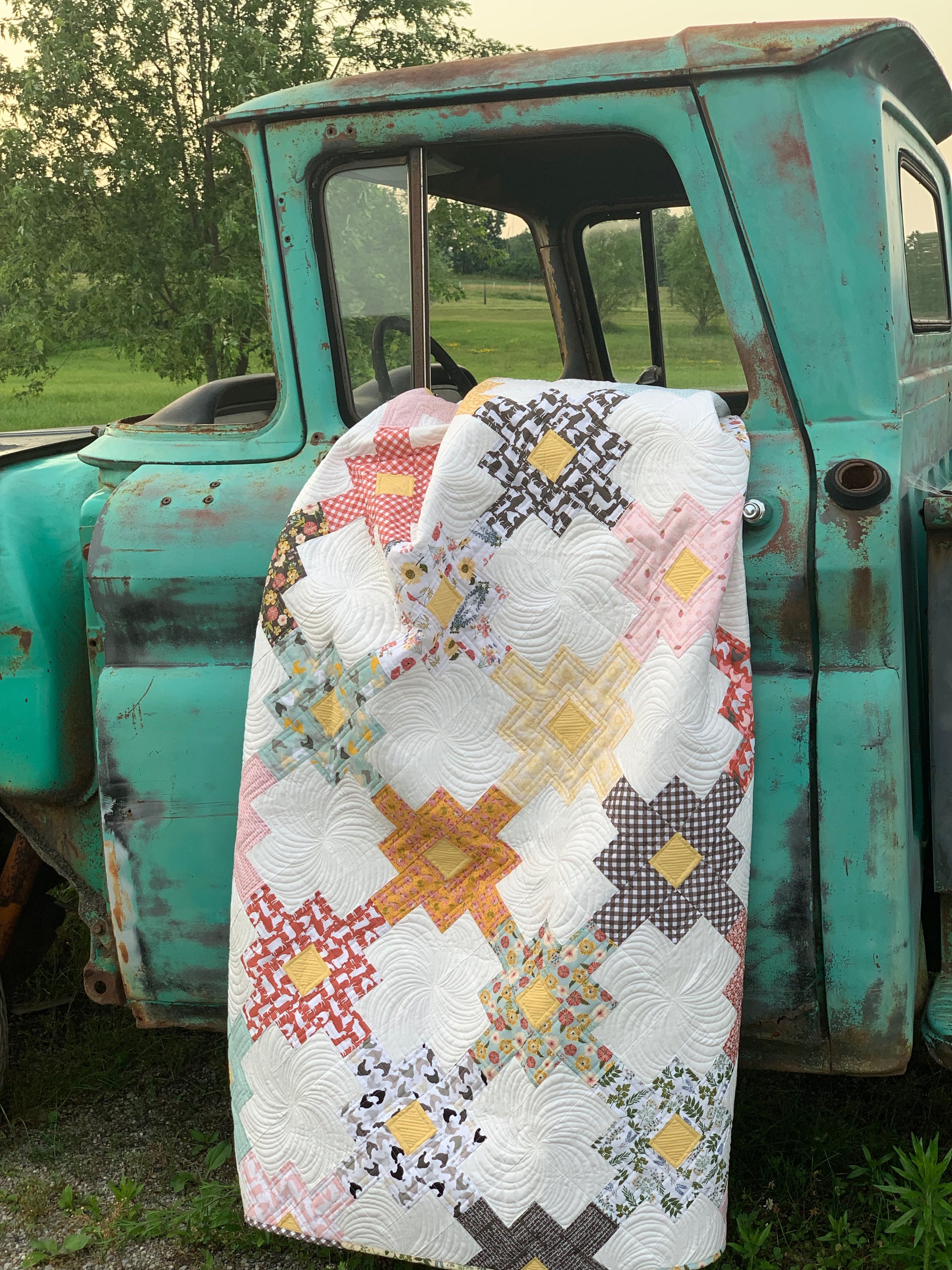 Colorful quilt with star pattern in yellow, pink, and red, draped over a vintage turquoise truck.