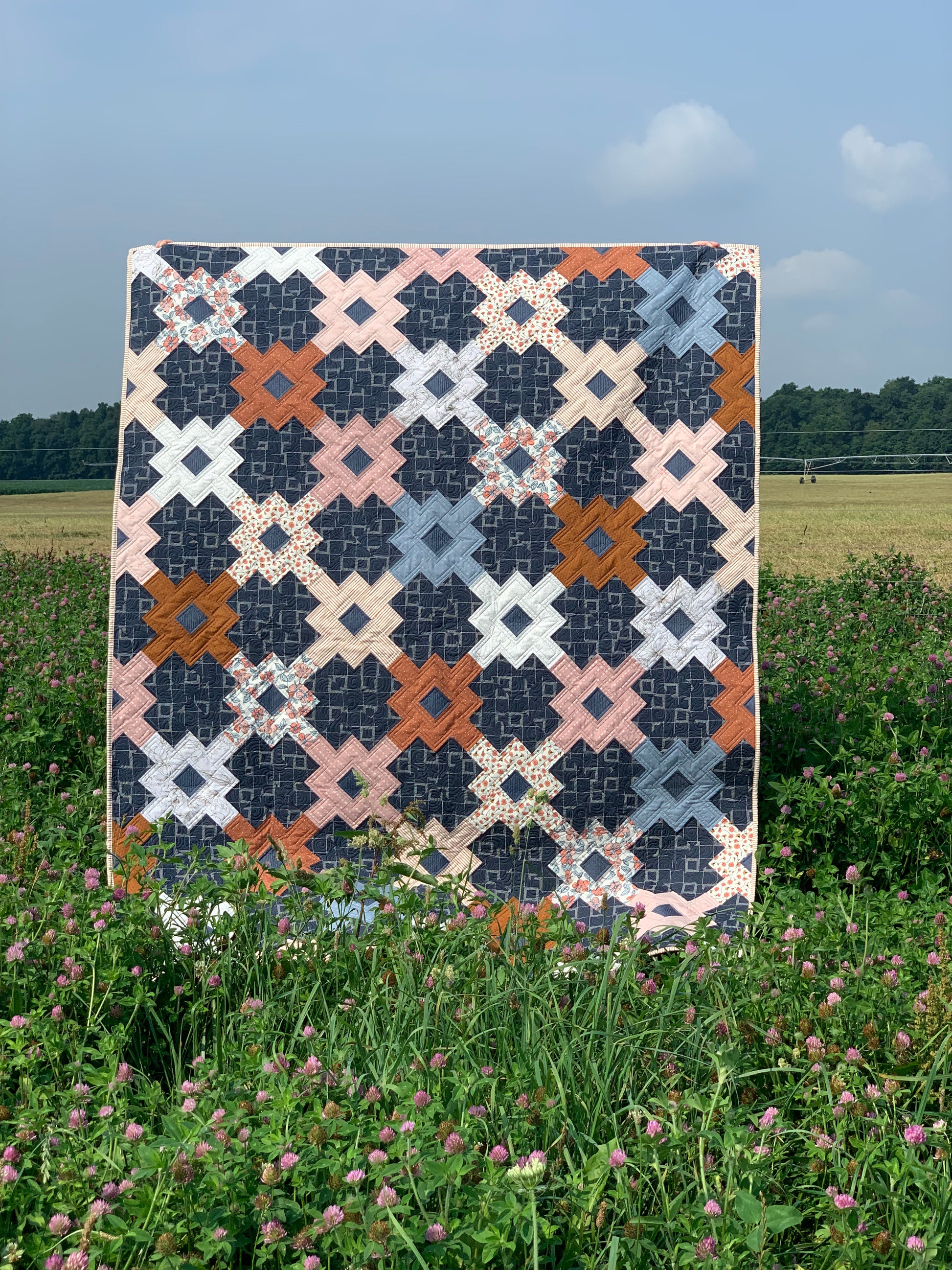 Colorful quilt featuring geometric patterns in navy, pink, and orange, beautifully displayed in a field.