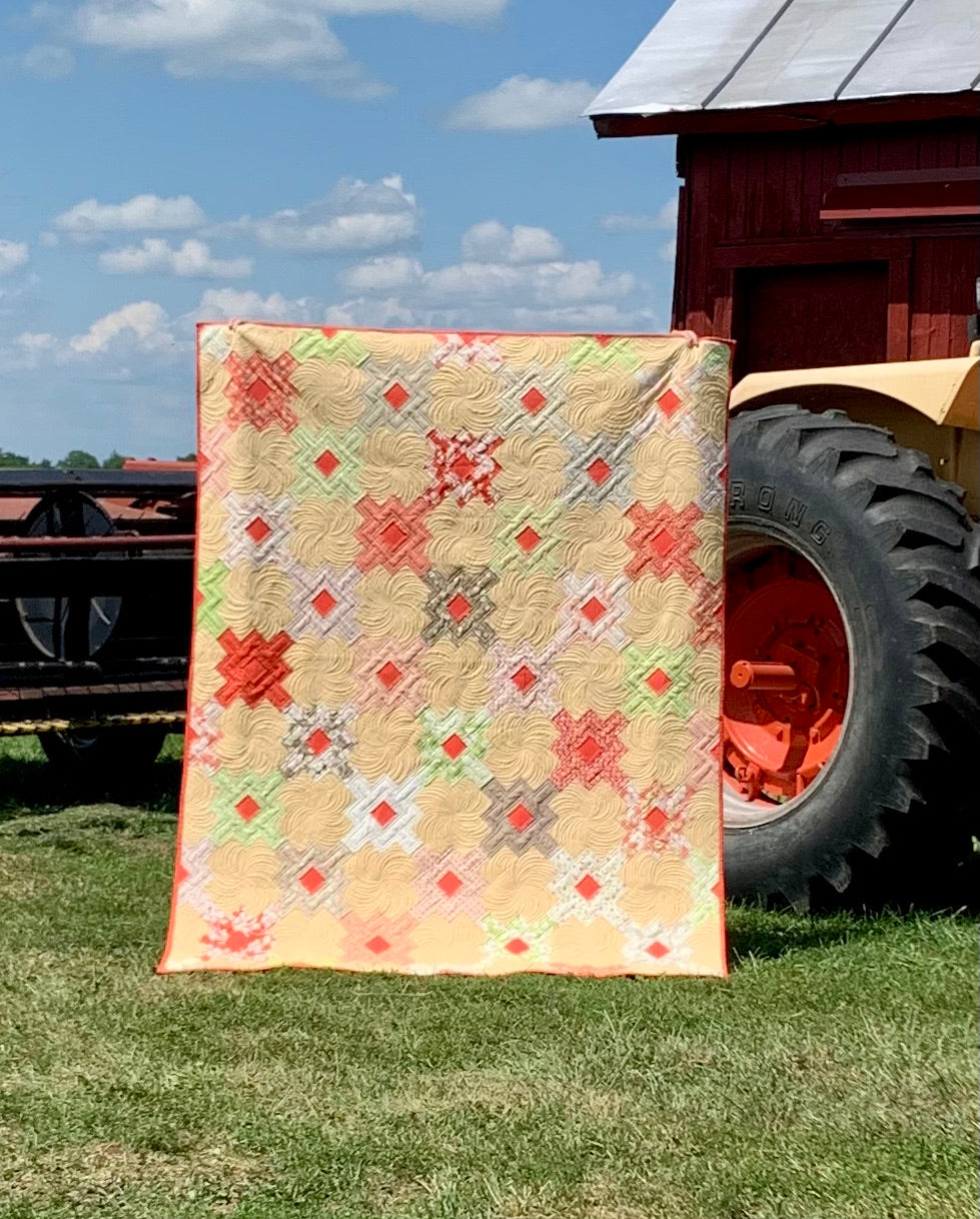 Colorful quilt featuring geometric patterns in orange, red, green, and beige, ideal for home decor or cozy gifts.