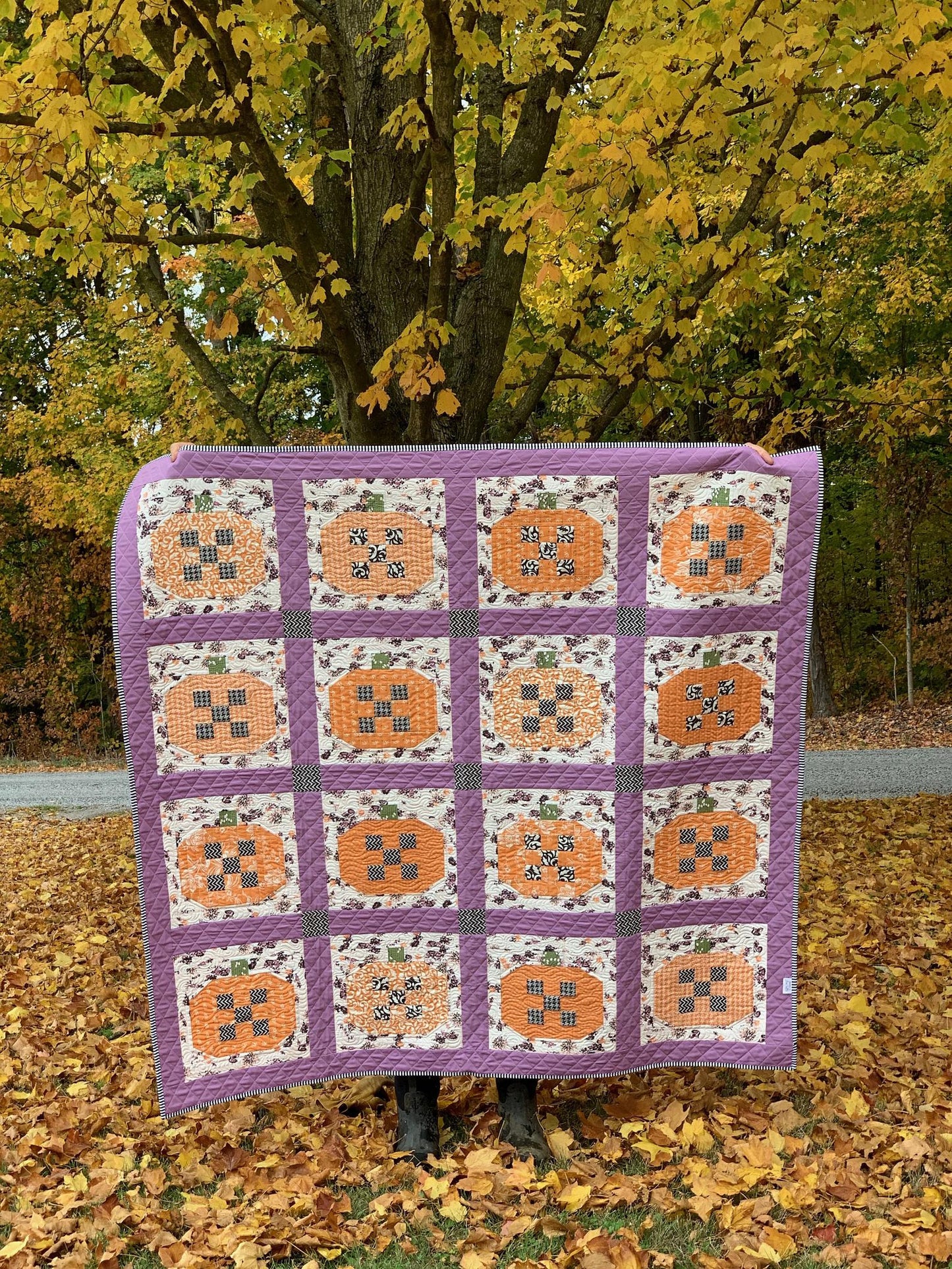 Handmade quilt featuring orange pumpkins, purple border, and floral patterns, perfect for autumn decor.