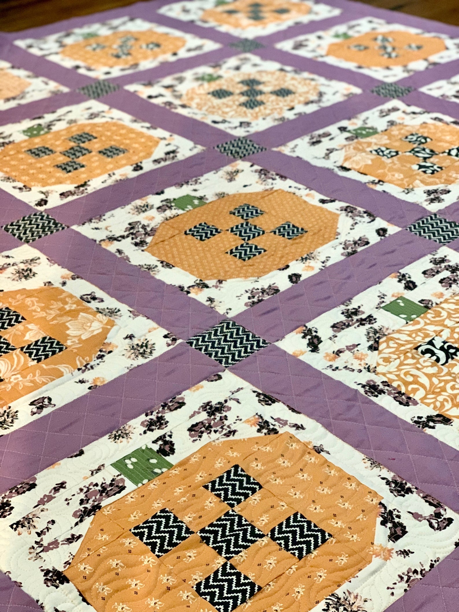 Colorful quilt with floral patterns, orange and purple patches, made from cotton fabric, perfect for home decor.