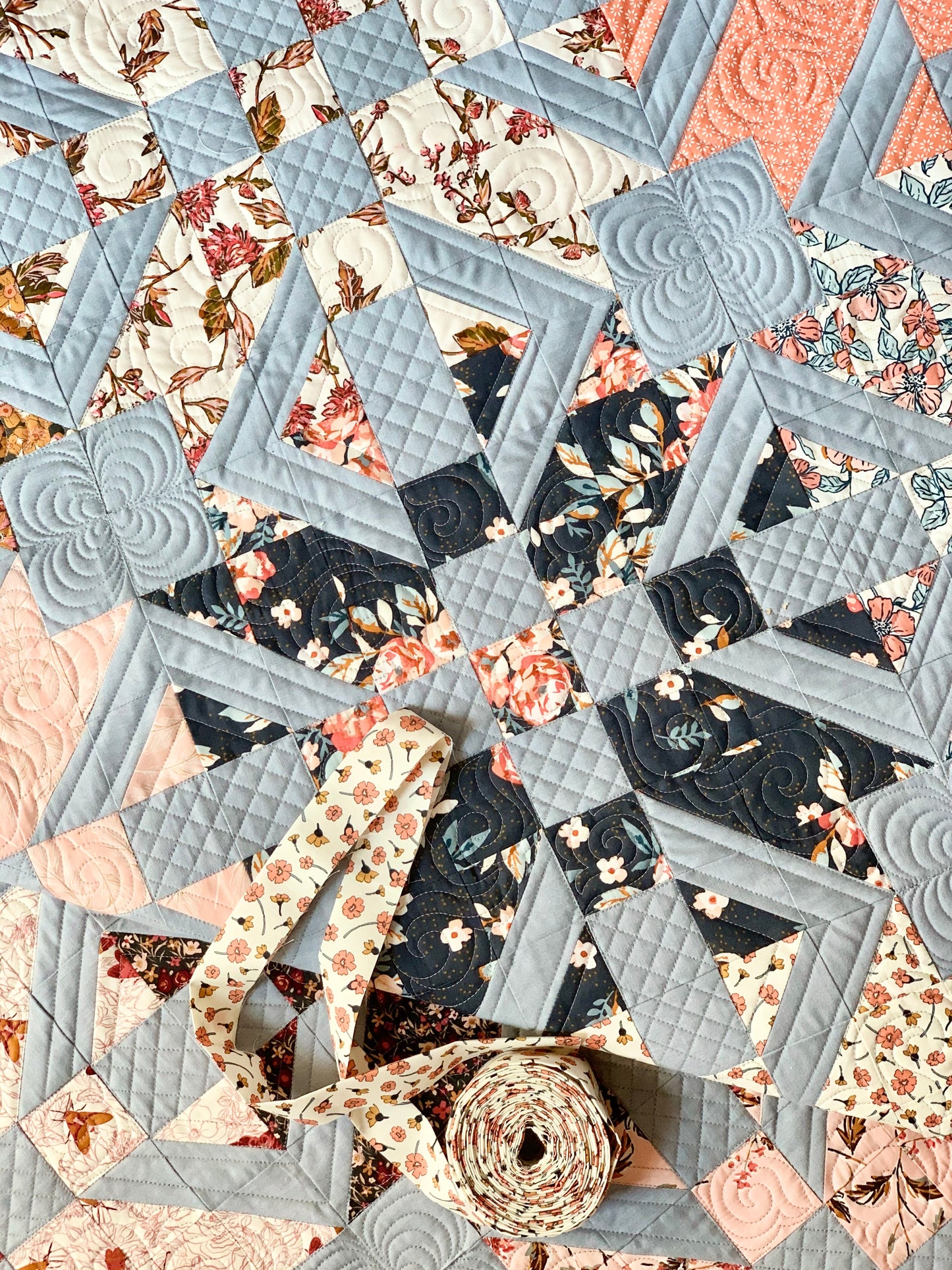 Light blue and floral quilt with intricate patterns, featuring rolled fabric strips for sewing projects.